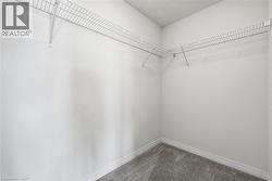 Interior closet featuring white walls, white wire shelving, white baseboards, and grey carpet flooring - 