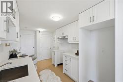 White kitchen featuring flat-panel cabinetry, brushed nickel hardware, light wood-finish flooring, a stainless steel sink, and a built-in oven hood - 