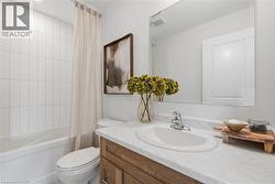 Bathroom featuring a white subway-tiled shower, white bathtub, wood-finish vanity with an integrated sink, polished chrome faucet, and a large wall-mounted mirror - 