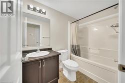 Full bathroom featuring a dark wood-finish vanity with an integrated sink, a rectangular mirror, and a three-bulb vanity light - 