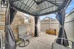 Private outdoor patio featuring a metal gazebo with privacy curtains, stone exterior wall, concrete flooring, and a lattice-topped fence - 