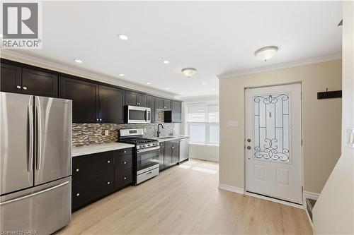 Kitchen featuring dark cabinetry, stainless steel appliances, a tile backsplash, and light wood-finish flooring - 309 Cope Street, Hamilton, ON - Indoor Photo Showing Kitchen With Stainless Steel Kitchen
