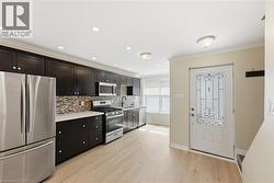 Kitchen featuring dark cabinetry, stainless steel appliances, a tile backsplash, and light wood-finish flooring - 