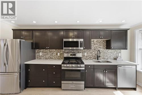 Kitchen featuring dark cabinetry, stainless steel appliances, a tile backsplash, and light wood-finish flooring - 309 Cope Street, Hamilton, ON - Indoor Photo Showing Kitchen With Stainless Steel Kitchen With Double Sink With Upgraded Kitchen