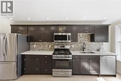 Kitchen featuring dark cabinetry, stainless steel appliances, a tile backsplash, and light wood-finish flooring - 