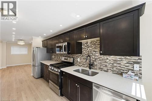 Kitchen featuring dark cabinetry, stainless steel appliances, a tile backsplash, and light wood-finish flooring - 309 Cope Street, Hamilton, ON - Indoor Photo Showing Kitchen With Stainless Steel Kitchen With Double Sink With Upgraded Kitchen