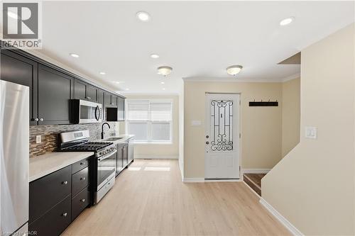 Kitchen featuring dark cabinetry, stainless steel appliances, a tile backsplash, and light wood-finish flooring - 309 Cope Street, Hamilton, ON - Indoor Photo Showing Kitchen