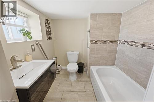 Bathroom featuring a modern vanity with integrated sink, tiled flooring, a standard toilet, and a bathtub with tiled surround and decorative accent band - 309 Cope Street, Hamilton, ON - Indoor Photo Showing Bathroom