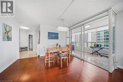 Open-concept living area featuring rich wood-finish flooring, a contemporary rectangular chandelier, and a separate sunroom with floor-to-ceiling windows - 