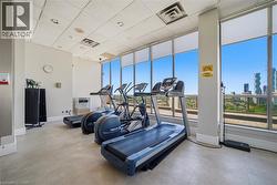 Fitness area with multiple cardio machines, large windows, roller shades, acoustic panel ceiling, and neutral flooring - 