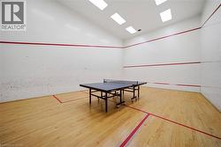 Indoor recreational room featuring hardwood flooring, white walls with red court lines, and overhead square lighting fixtures - 