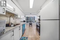 Galley kitchen featuring white cabinetry, light granite-style countertops, an undermount stainless steel sink with a gooseneck faucet, light tile flooring, and integrated appliances - 