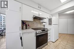 Modern kitchen featuring white cabinetry with brushed nickel hardware, stone-finish countertops, stainless steel appliances, and a tiled backsplash - 