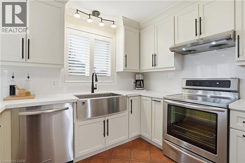 Kitchen featuring white shaker-style cabinetry, stainless steel appliances, a farmhouse sink with a matte black faucet, white countertops, and a white tile backsplash - 56 Mccaffery Crescent, St. Catharines, ON 