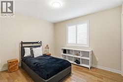 Light-filled room featuring wood-finish flooring, neutral wall tones, a window with plantation shutters, a contemporary ceiling light fixture, and white baseboards - 