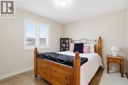 Bright room featuring a window with white louvered shutters, light beige wall paint, wood-finish flooring, and white baseboards - 