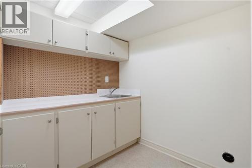 Utility room featuring extensive white cabinetry, a built-in stainless steel sink, a pegboard wall, ample countertop space, and overhead fluorescent lighting - 56 Mccaffery Crescent, St. Catharines, ON 