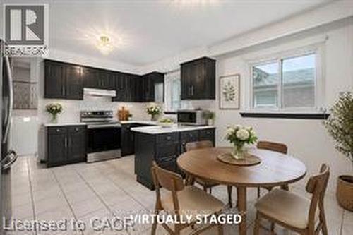 Kitchen featuring dark cabinetry, stainless steel appliances, a white tile backsplash, a center island with countertop, and light-toned floor tiling - 396 Pinemeadow Avenue, Mississauga, ON 
