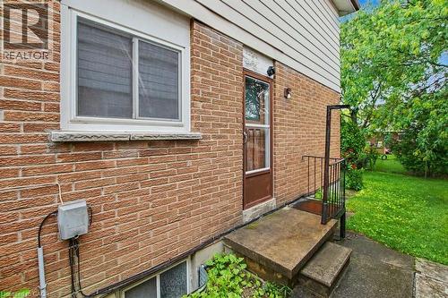 Brick exterior with white siding above, featuring a concrete stoop with metal railing, an exterior door, and a horizontal sliding window with stone sill - 396 Pinemeadow Avenue, Mississauga, ON 