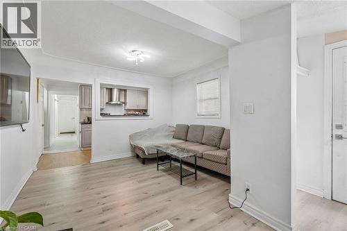 Bright living area featuring light wood-finish flooring, a ceiling-mounted light fixture, and a window with blinds - 43 Whitfield Avenue, Hamilton, ON 