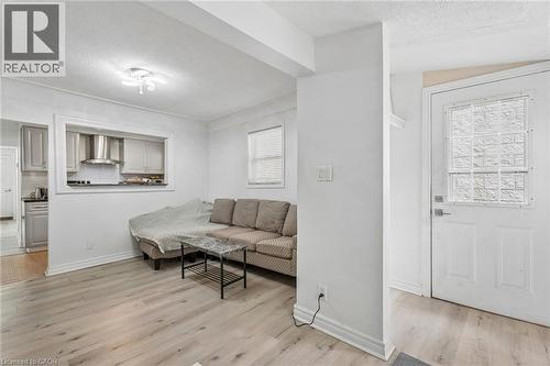 Open-concept living area with light wood-finish flooring, a white paneled entry door with decorative glass, and a large pass-through window to the kitchen - 43 Whitfield Avenue, Hamilton, ON 