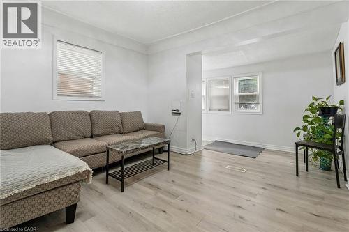Bright living area featuring light wood-finish flooring, white walls, and multiple windows with horizontal blinds - 43 Whitfield Avenue, Hamilton, ON 