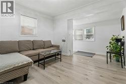 Bright living area featuring light wood-finish flooring, white walls, and multiple windows with horizontal blinds - 