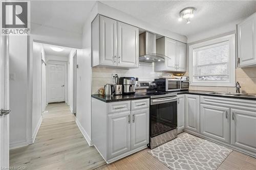Efficient kitchen featuring light gray cabinetry, dark countertops, a stainless steel range with overhead hood, and light wood-finish flooring - 43 Whitfield Avenue, Hamilton, ON 