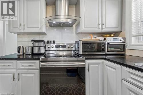 Kitchen featuring light-colored cabinetry with silver hardware, dark countertops, and a stainless steel range with a matching range hood - 43 Whitfield Avenue, Hamilton, ON 