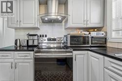 Kitchen featuring light-colored cabinetry with silver hardware, dark countertops, and a stainless steel range with a matching range hood - 