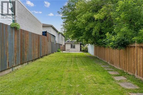 Expansive grassy yard area featuring a privacy fence, stepping stone pathway, and mature trees - 43 Whitfield Avenue, Hamilton, ON 