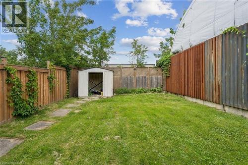 Expansive grassy yard with concrete paver pathway, featuring a metal storage shed and surrounding wood-panel fencing - 43 Whitfield Avenue, Hamilton, ON 
