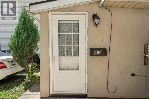 Entryway featuring a white paneled door with window inserts, stucco exterior, and an exterior wall light fixture - 43 Whitfield Avenue, Hamilton, ON 