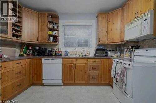 Kitchen featuring wood-finish cabinetry, integrated wine storage, an overhead microwave, tile backsplash, and a double basin sink - 98 Brubacher Street, Kitchener, ON 