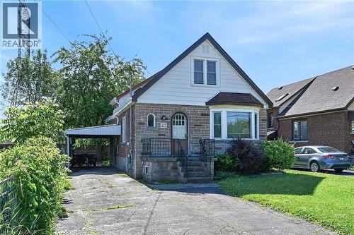 Stone and siding exterior featuring a covered carport, bay window, front entryway with a wrought iron railing, and an arched storm door - 83 Aberfoyle Avenue, Hamilton, ON 
