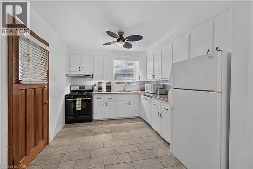 Kitchen featuring white cabinetry, stone-look countertops, a black range with exhaust hood, and light tile flooring - 83 Aberfoyle Avenue, Hamilton, ON 