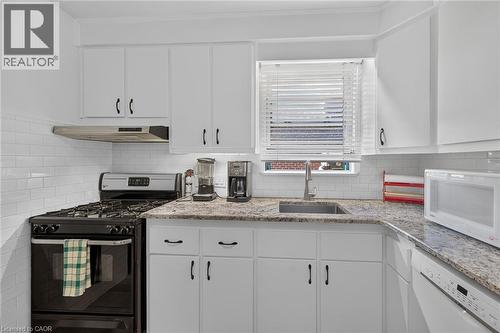 Kitchen featuring white cabinetry, subway tile backsplash, granite countertops, an undermount sink with a gooseneck faucet, and a black range with a stainless steel vent hood - 83 Aberfoyle Avenue, Hamilton, ON 