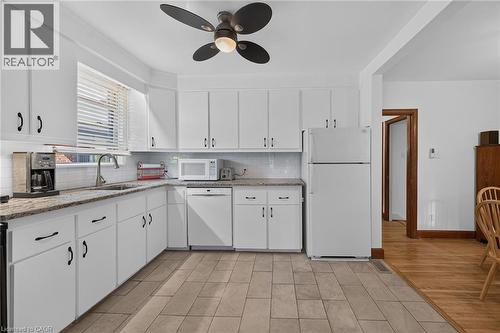 Bright kitchen featuring white cabinetry, granite-finish countertops, tile flooring, a subway tile backsplash, and a ceiling fan - 83 Aberfoyle Avenue, Hamilton, ON 