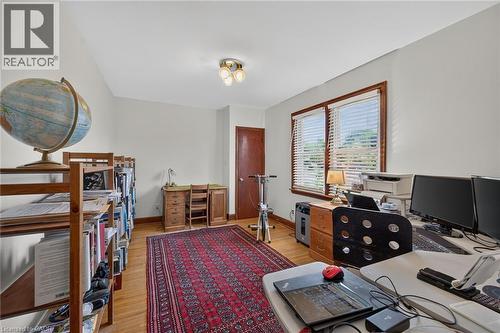 Hardwood flooring throughout this room, featuring a double window with wood trim, a paneled door, and a flush-mount ceiling light fixture - 83 Aberfoyle Avenue, Hamilton, ON 