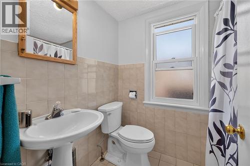 Pedestal sink with chrome faucet, light-colored square wall tiles, and wood-framed mirror - 83 Aberfoyle Avenue, Hamilton, ON 