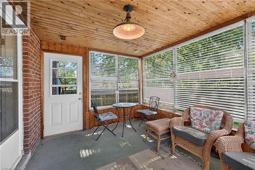 Enclosed porch featuring a wood-panel ceiling, brick wall, wood-paneled accent wall, screened windows with blinds, and a white exterior door with window panes - 83 Aberfoyle Avenue, Hamilton, ON 