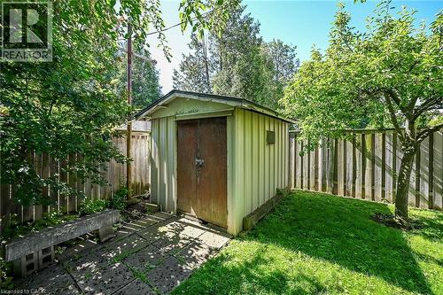 Backyard storage shed with paneled siding, double doors, and a small window, bordered by a wooden privacy fence, mature trees, and a grass lawn - 83 Aberfoyle Avenue, Hamilton, ON 