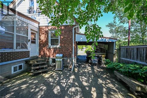 Brick exterior featuring a covered carport, concrete patio, and mature perimeter fencing - 83 Aberfoyle Avenue, Hamilton, ON 