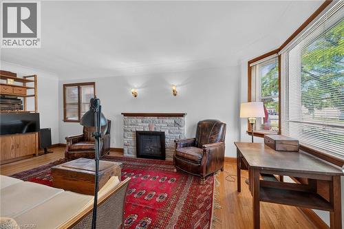 Living area featuring a stone-clad fireplace with a dark metal insert, hardwood flooring, and a bay window with wood trim - 83 Aberfoyle Avenue, Hamilton, ON 