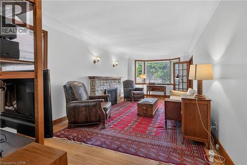 Living area featuring a stone-clad fireplace, wood-finish flooring, and bay windows - 83 Aberfoyle Avenue, Hamilton, ON 