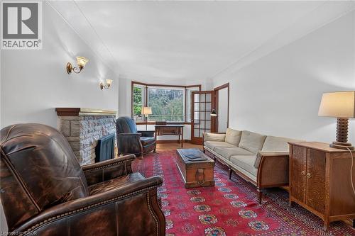 Spacious living area featuring a stone-clad fireplace with wood mantel, wall sconces, wood-frame bay windows, and wood-finish flooring - 83 Aberfoyle Avenue, Hamilton, ON 