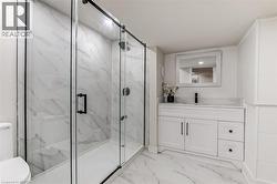 Modern bathroom featuring a glass-enclosed shower with matte black hardware, white tile walls, and a white vanity with a rectangular sink and matte black faucet - 