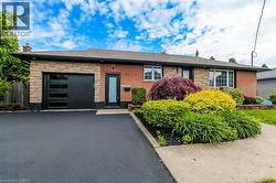Brick and stone facade bungalow featuring a modern black garage door with rectangular windows, an asphalt driveway, and a concrete walkway - 