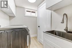 Dedicated utility space featuring ample upper cabinetry, a stainless steel sink with a gooseneck faucet, light wood-finish flooring, and a window for natural illumination - 