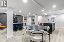 Brightly lit lower level featuring recessed lighting, light wood-finish flooring, a built-in entertainment area with a textured accent wall, and a kitchen island with an integrated sink and matte blac - 